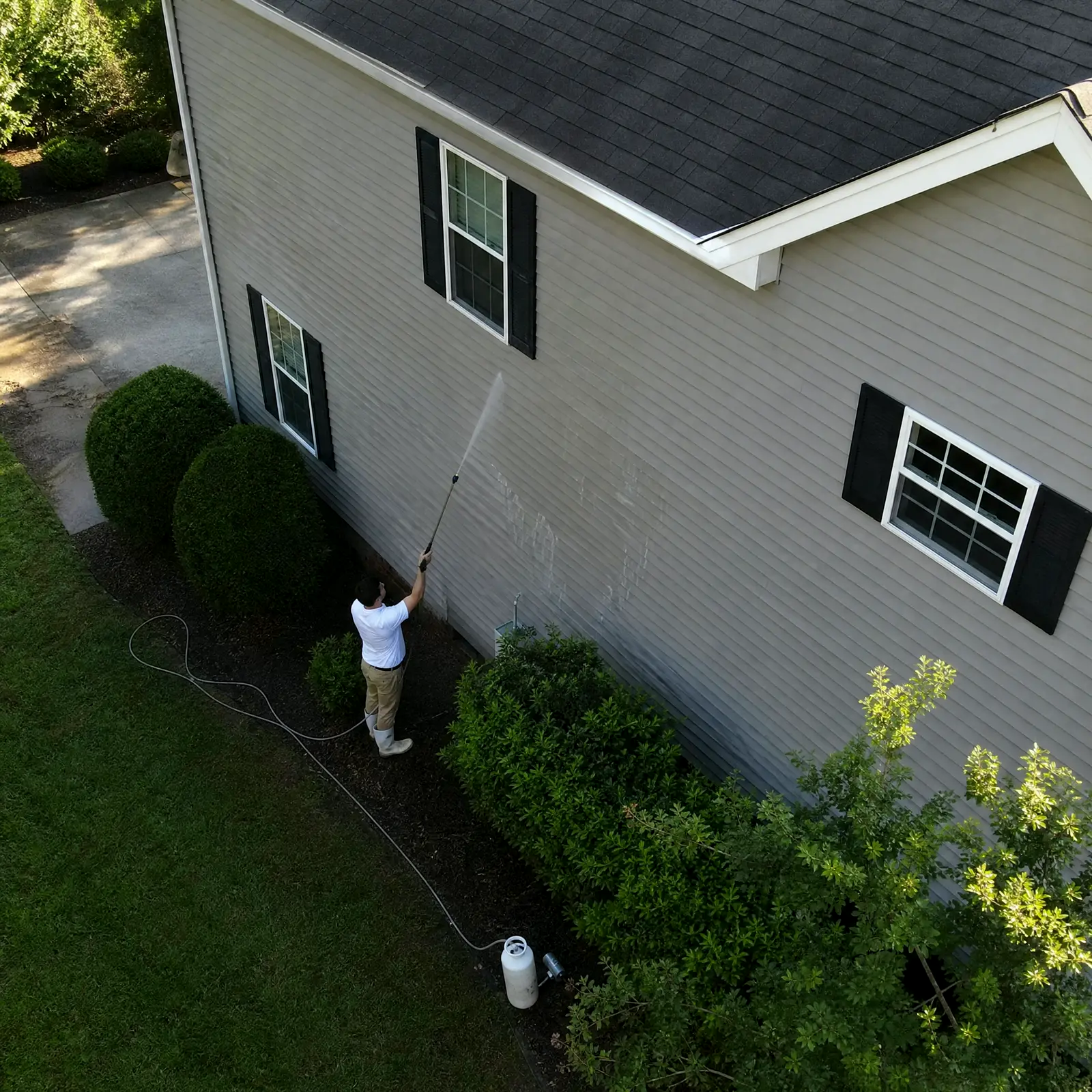 Technician soft washing a roof and vinyl siding at low pressure