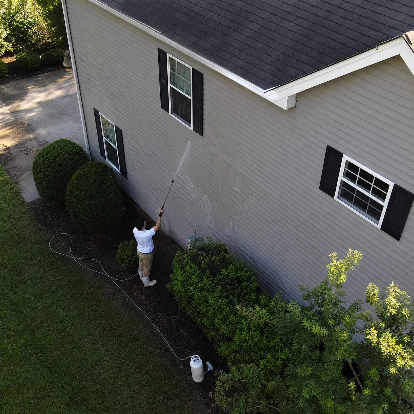 Technician soft washing a roof and vinyl siding at low pressure