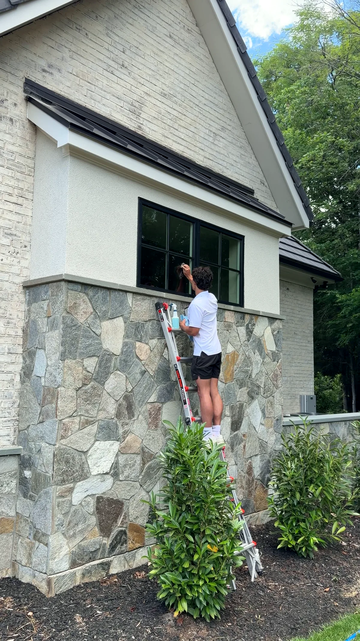 Coastal Exteriors technician hand-detailing a window from a ladder