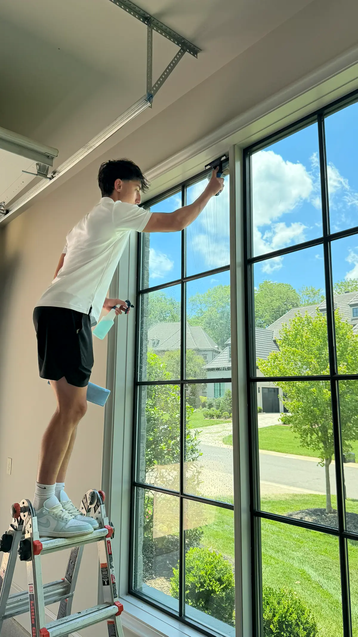 Coastal Exteriors technician cleaning interior window panes from a ladder in a Charlotte home