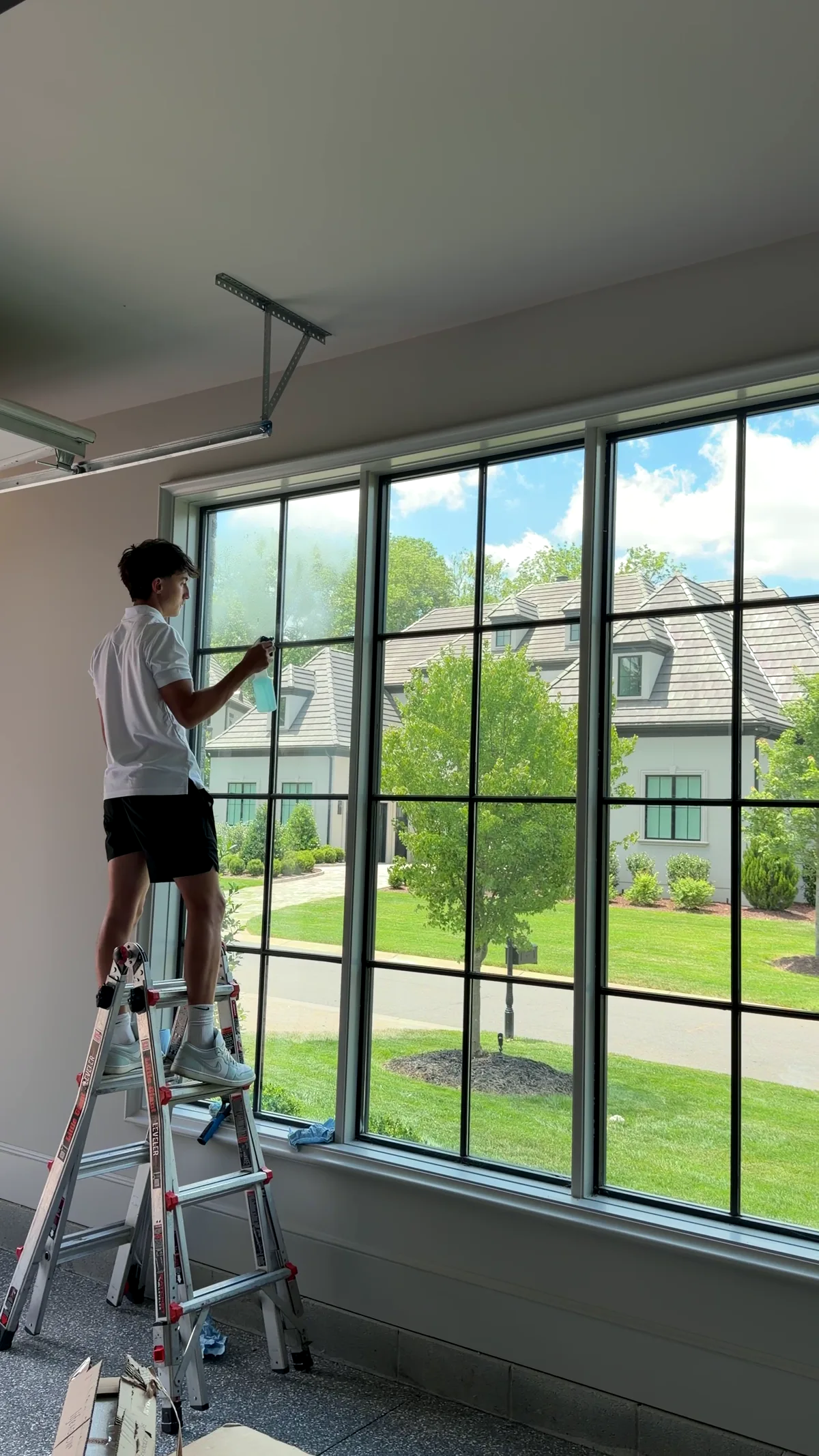 Coastal Exteriors technician cleaning interior window panes from a ladder in a Charlotte home